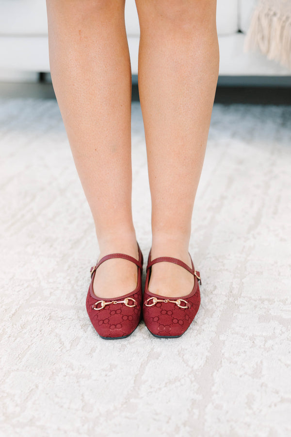 Wine-colored flats with a monogram pattern and gold buckle detail.