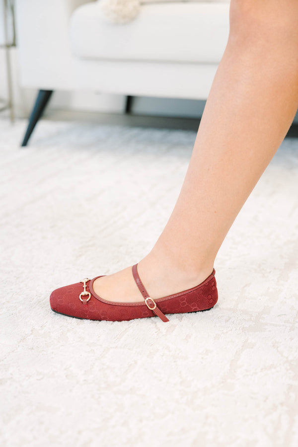 Wine-colored flats with a monogram pattern and gold buckle detail.