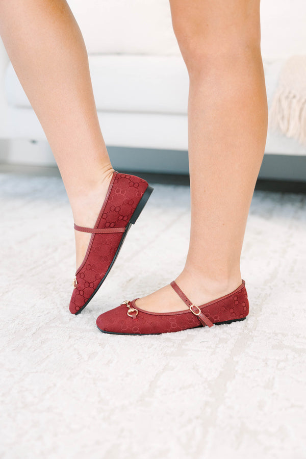 Wine-colored flats with a monogram pattern and gold buckle detail.