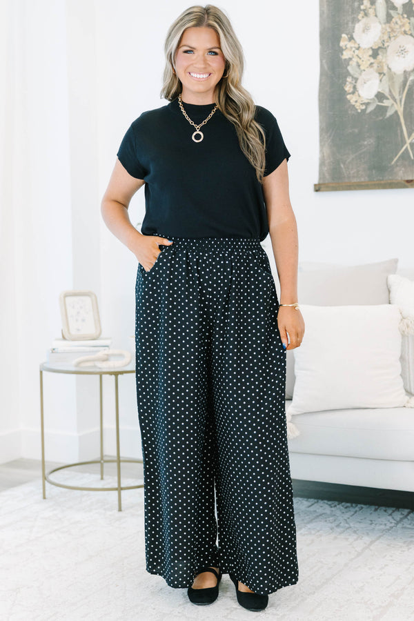 Plus size black wide-leg pants with white polka dots featuring a flowy fit and smocked waist.