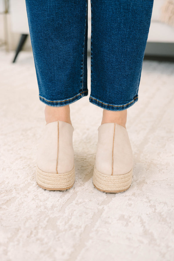 A person wearing sand-colored platform wedge mules with a woven jute sole
