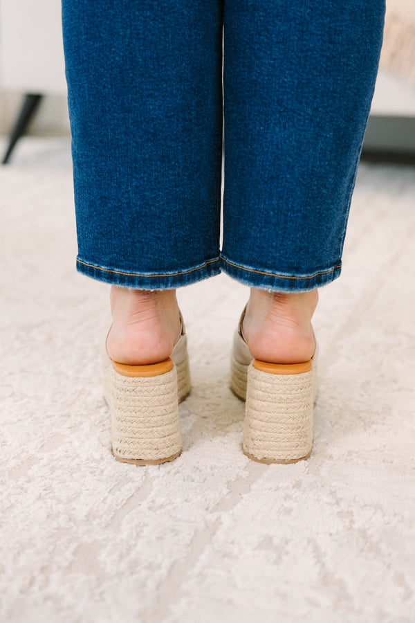 A person wearing sand-colored platform wedge mules with a woven jute sole