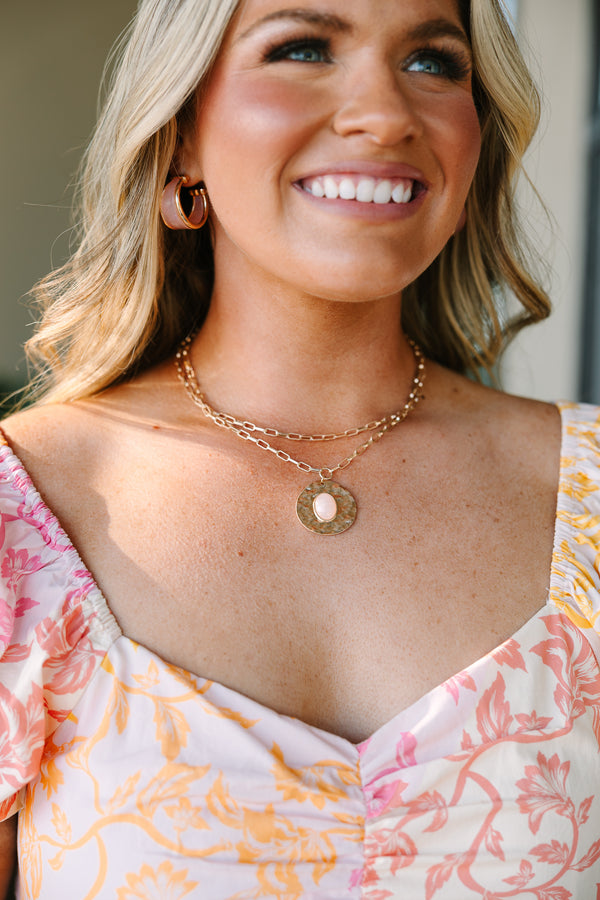 Layered gold chain necklace with a hammered disc pendant featuring a light pink oval stone.