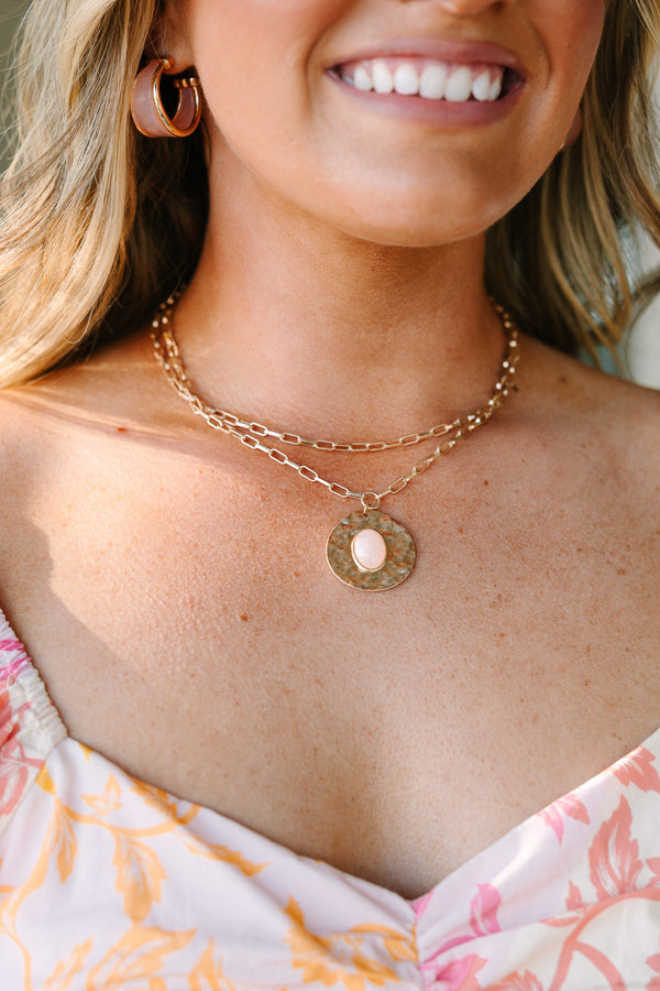 Layered gold chain necklace with a hammered disc pendant featuring a light pink oval stone.