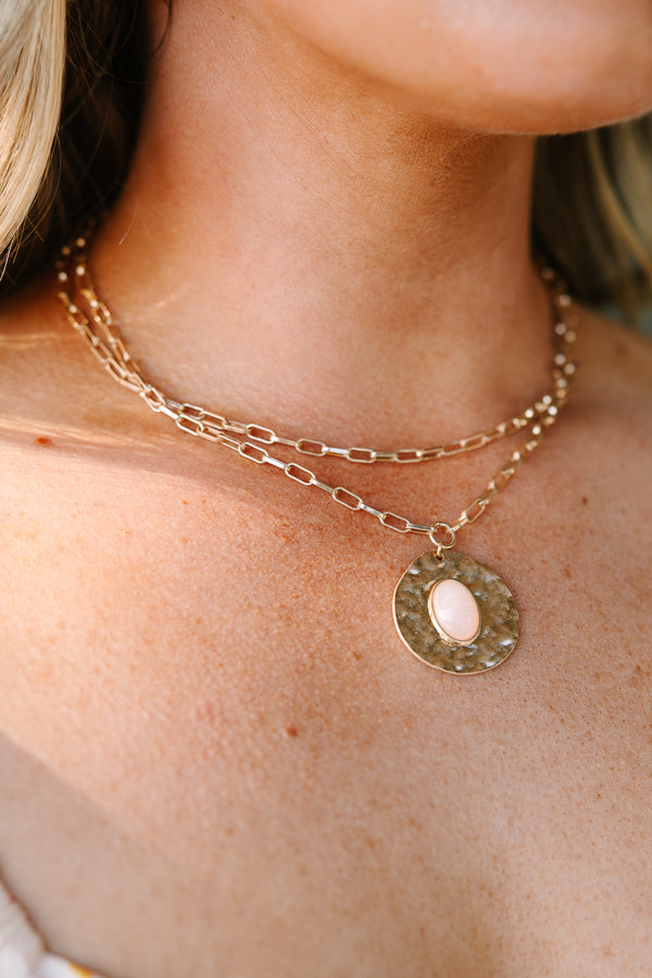 Layered gold chain necklace with a hammered disc pendant featuring a light pink oval stone.