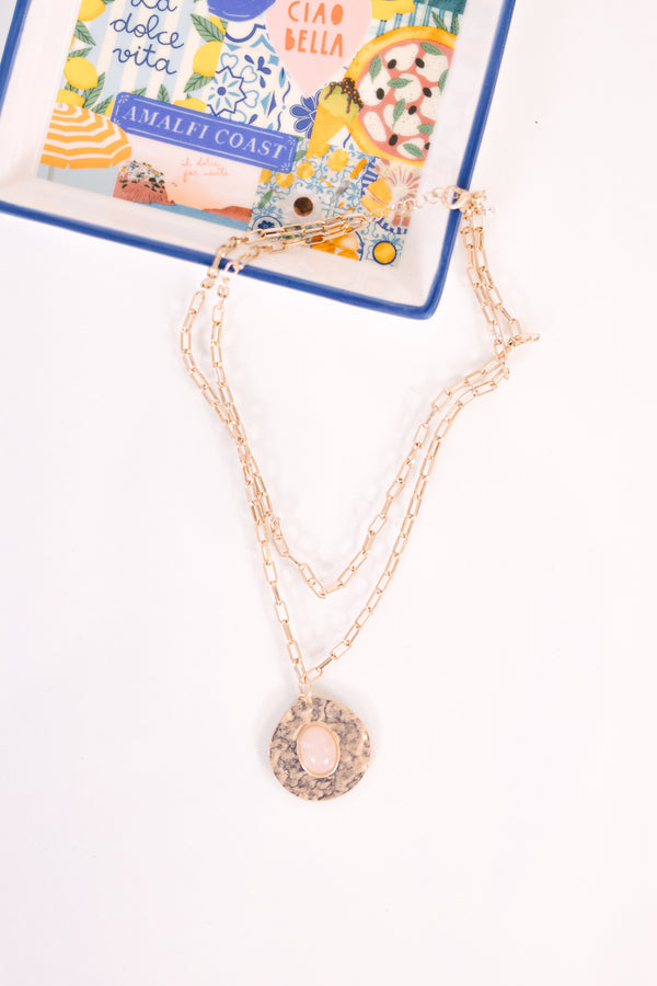 Layered gold chain necklace with a hammered disc pendant featuring a light pink oval stone.