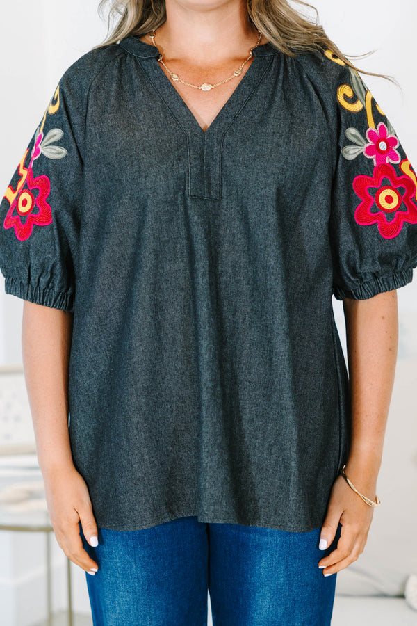 Plus Size black denim top with a v-neckline and colorful floral embroidery on puff sleeves.