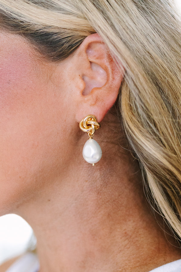 Gold knot stud earrings featuring dangling white baroque pearls.