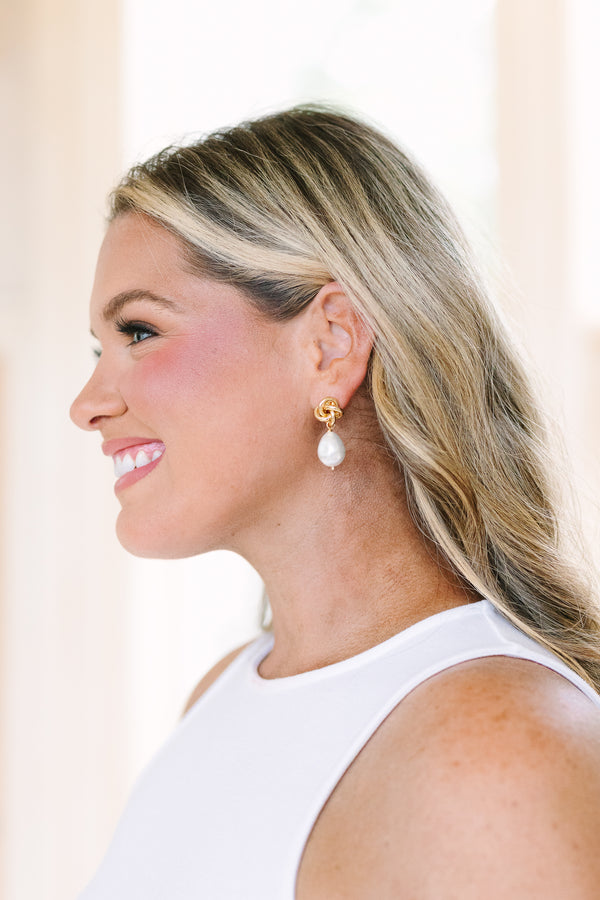 Gold knot stud earrings featuring dangling white baroque pearls.