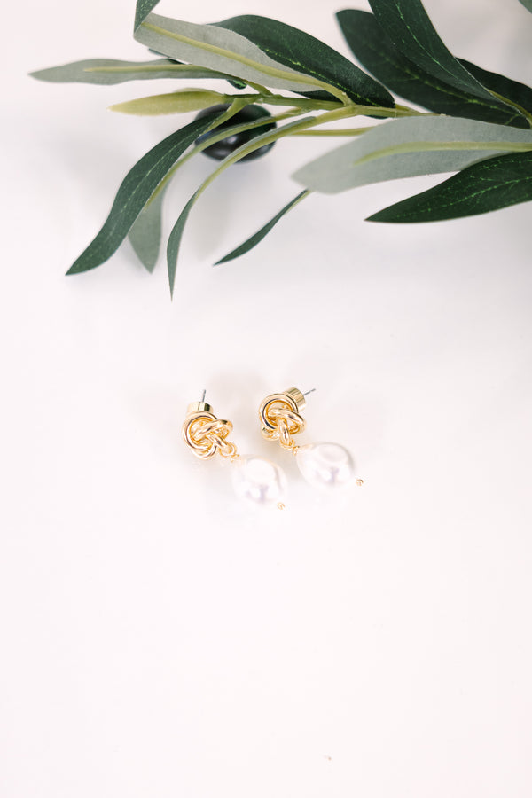 Gold knot stud earrings featuring dangling white baroque pearls.