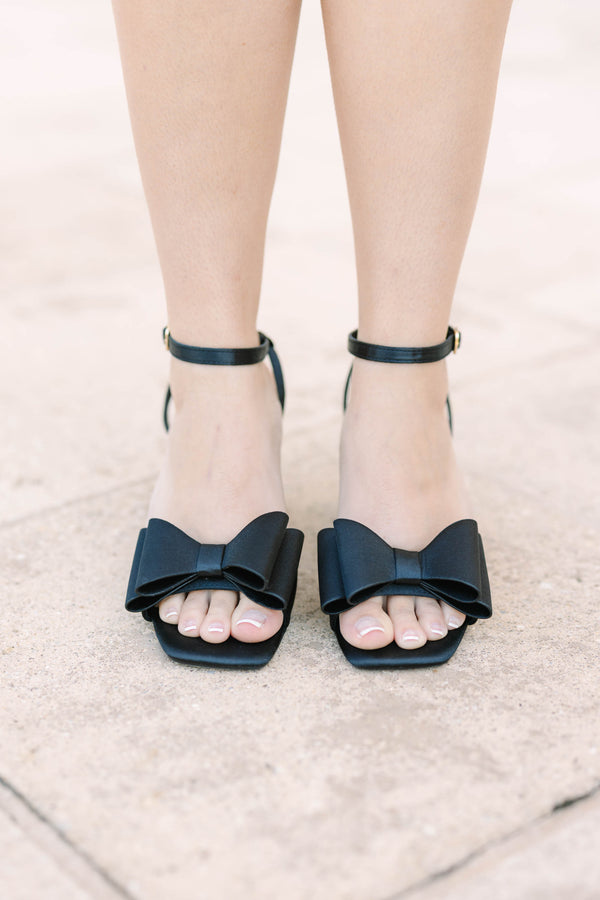 Plus size black satin block heels with a bow detail and adjustable ankle strap.