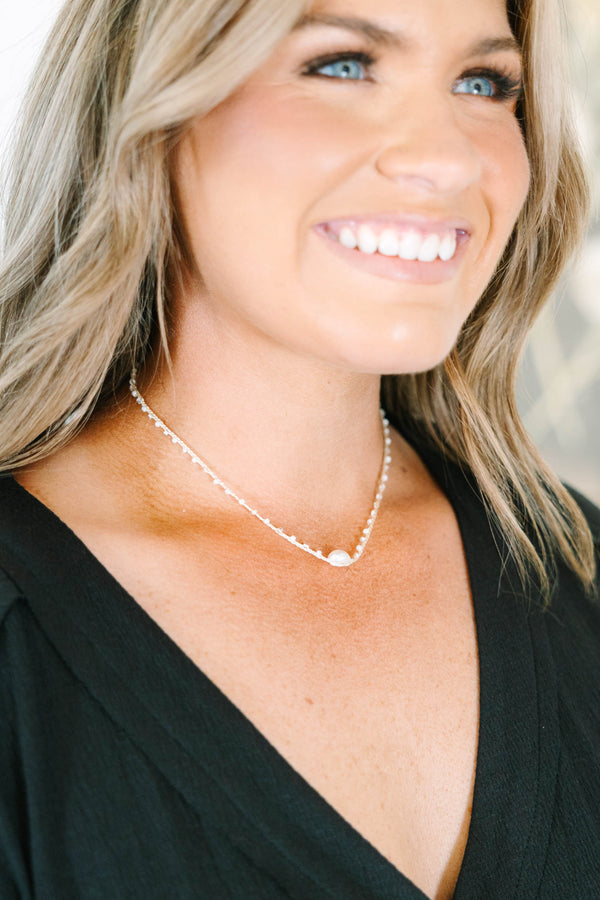 Delicate gold chain necklace with small white beads and a central pearl accent.