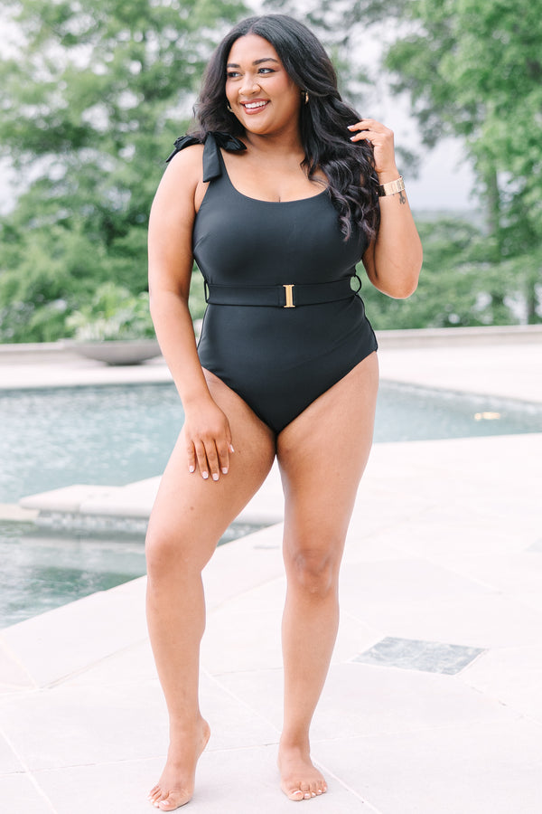 Plus Size black one-piece swimsuit with adjustable tie straps and a gold-buckled waist belt.