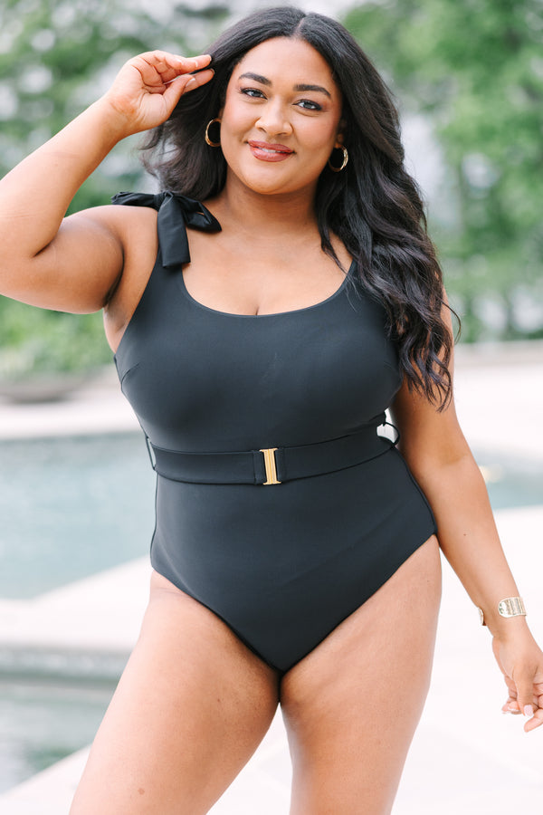 Plus Size black one-piece swimsuit with adjustable tie straps and a gold-buckled waist belt.