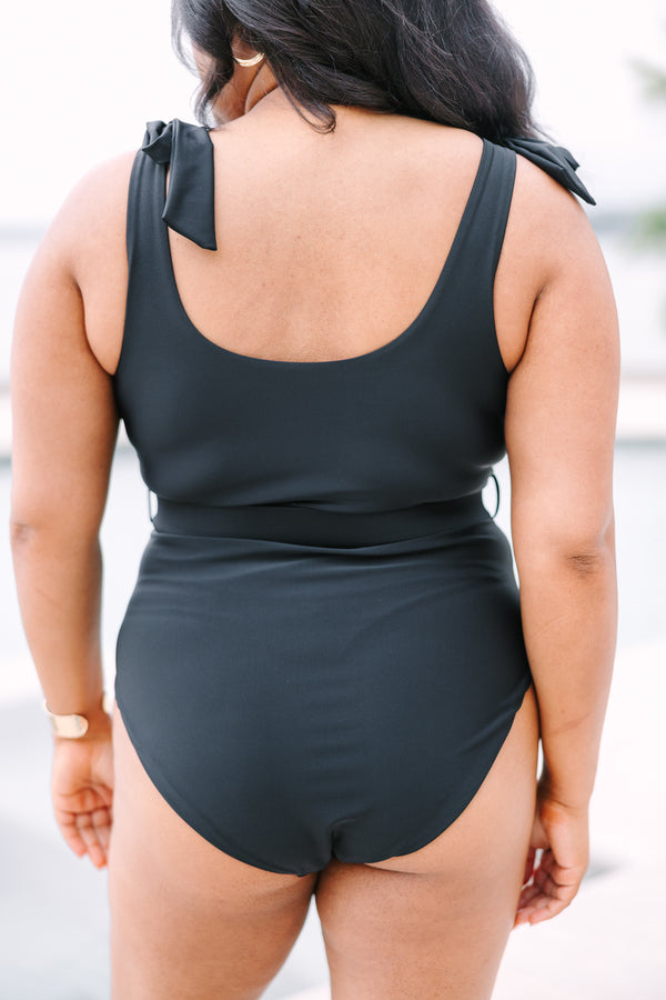 Plus Size black one-piece swimsuit with adjustable tie straps and a gold-buckled waist belt.