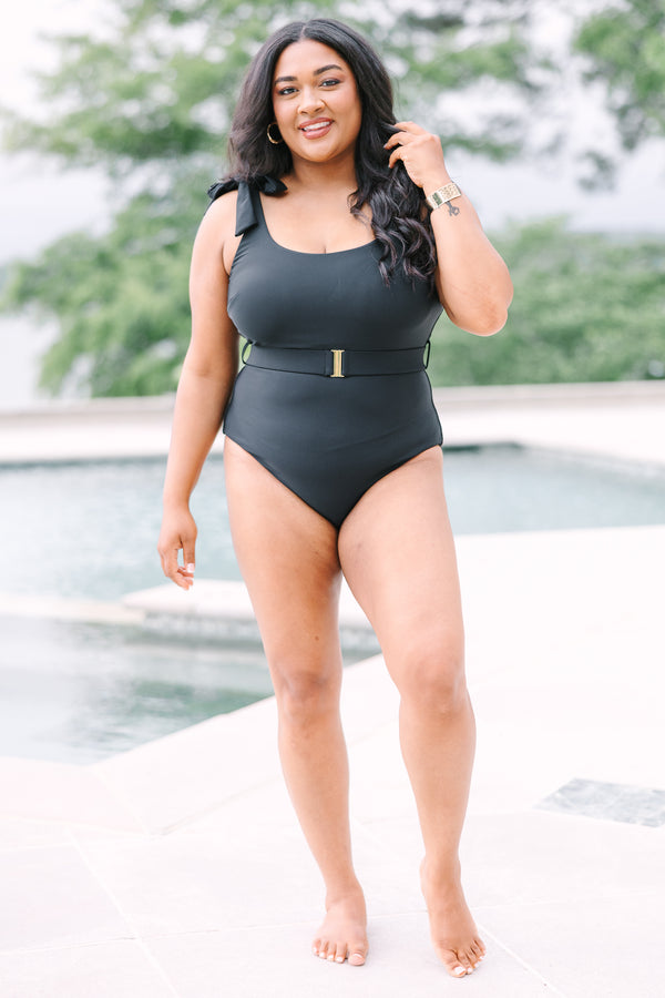 Plus Size black one-piece swimsuit with adjustable tie straps and a gold-buckled waist belt.