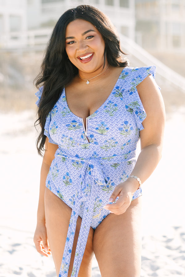Chic Soul plus size clothing, blue one piece bathing suit with flutter sleeves a deep neckline that features a gold v inset as well as a belt that ties in a bow around the waist and blue and green floral block pattern throughout 
