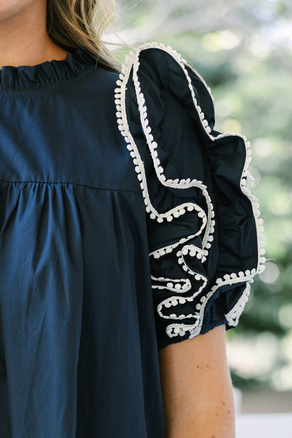 Navy cotton dress featuring a high ruffled neckline and tiered ruffle sleeves with white pom-pom trim.