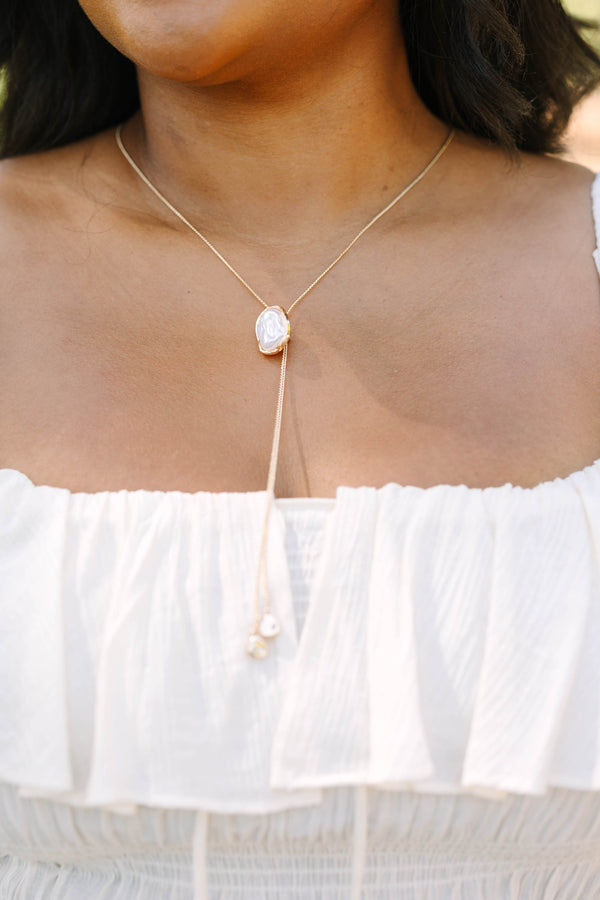 Plus Size white off-the-shoulder ruffled top with a gold lariat necklace featuring a pearl pendant.