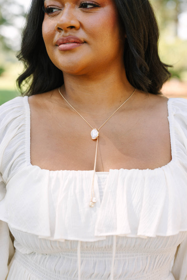 Plus Size white off-the-shoulder ruffled top with a gold lariat necklace featuring a pearl pendant.