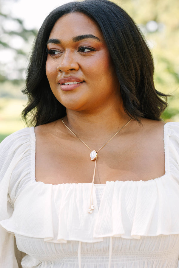 Plus Size white off-the-shoulder ruffled top with a gold lariat necklace featuring a pearl pendant.