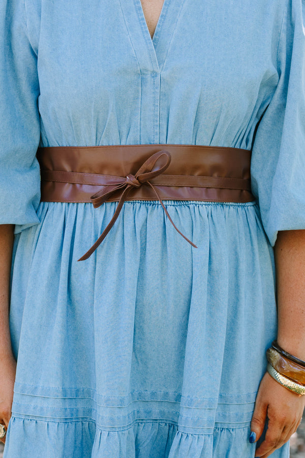 Plus Size brown faux leather wrap belt tied in a bow over a light blue denim dress.