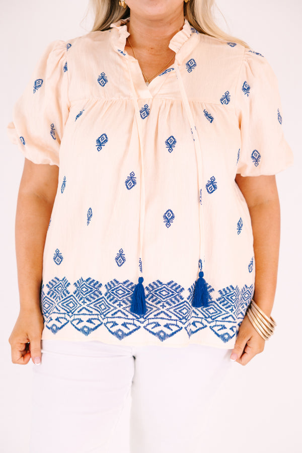Chic Soul plus size clothing, Beige short-sleeve blouse with a relaxed, flowy fit, featuring blue embroidered geometric patterns, a ruffled split neckline with tie tassels, and a decorative blue border along the hem.
