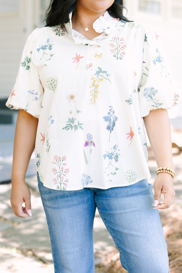 Ivory floral blouse with a relaxed fit, featuring a ruffled collar, short puff sleeves, and a lightweight woven fabric with a delicate multicolor botanical print.