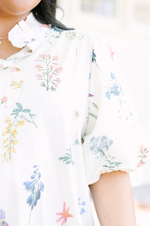 Ivory floral blouse with a relaxed fit, featuring a ruffled collar, short puff sleeves, and a lightweight woven fabric with a delicate multicolor botanical print.