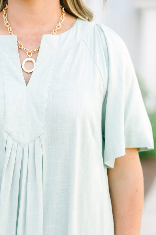 Short-sleeve sage green mini dress with a notched neckline and pleated front detailing.