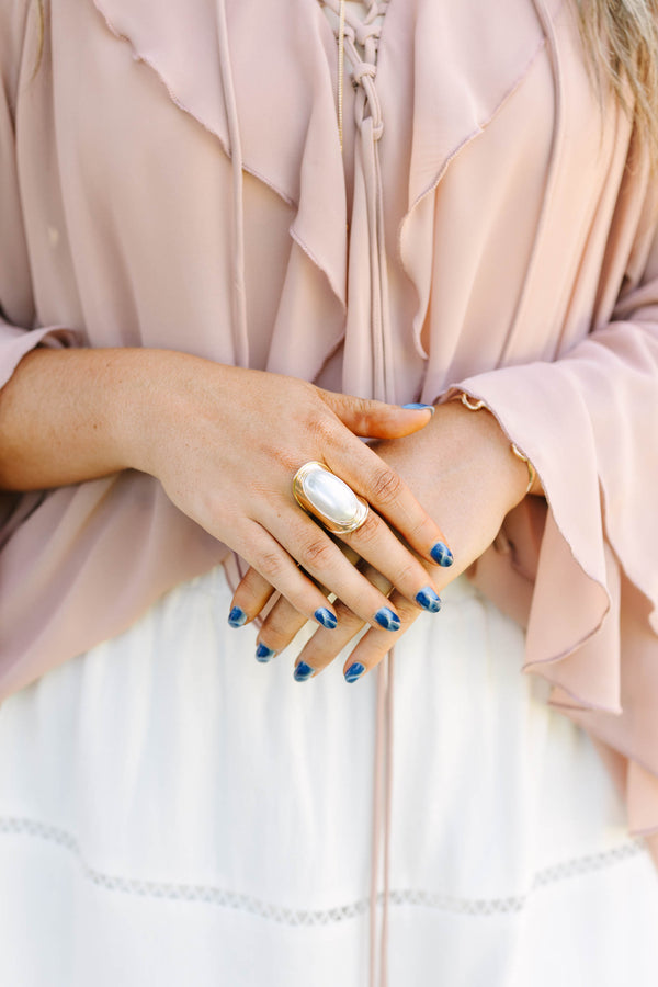 Plus Size gold ring with a large oval white pearl, worn with a ruffled pink blouse and white skirt.