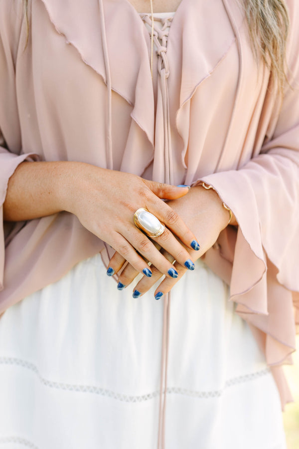 Plus Size gold ring with a large oval white pearl, worn with a ruffled pink blouse and white skirt.