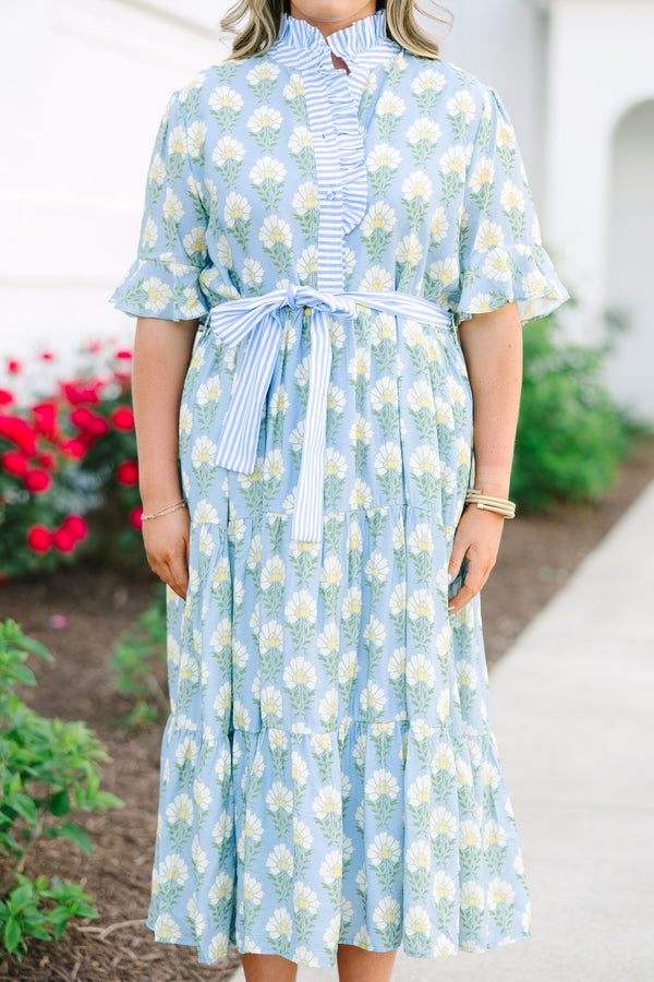 Blue floral maxi dress with short sleeves that flare out a blue multi floral pattern and a blue belt that ties into a bow that goes around the waist as blue ruffling details going along the neckline 