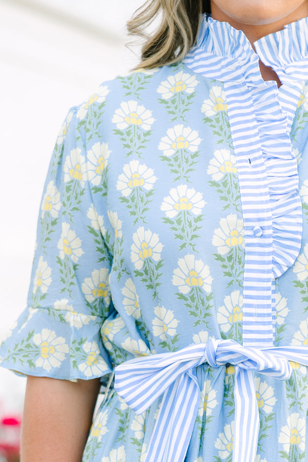 Blue floral maxi dress with short sleeves that flare out a blue multi floral pattern and a blue belt that ties into a bow that goes around the waist as blue ruffling details going along the neckline 