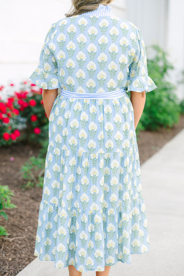 Blue floral maxi dress with short sleeves that flare out a blue multi floral pattern and a blue belt that ties into a bow that goes around the waist as blue ruffling details going along the neckline 