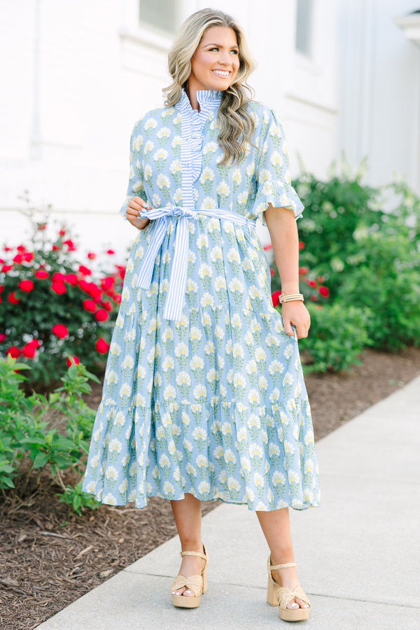 Blue floral maxi dress with short sleeves that flare out a blue multi floral pattern and a blue belt that ties into a bow that goes around the waist as blue ruffling details going along the neckline 