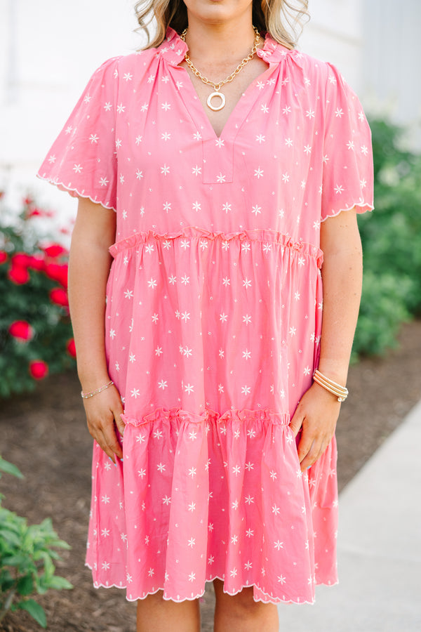 Pink tiered shift dress with white floral embroidery, a split neckline, and scalloped edges.