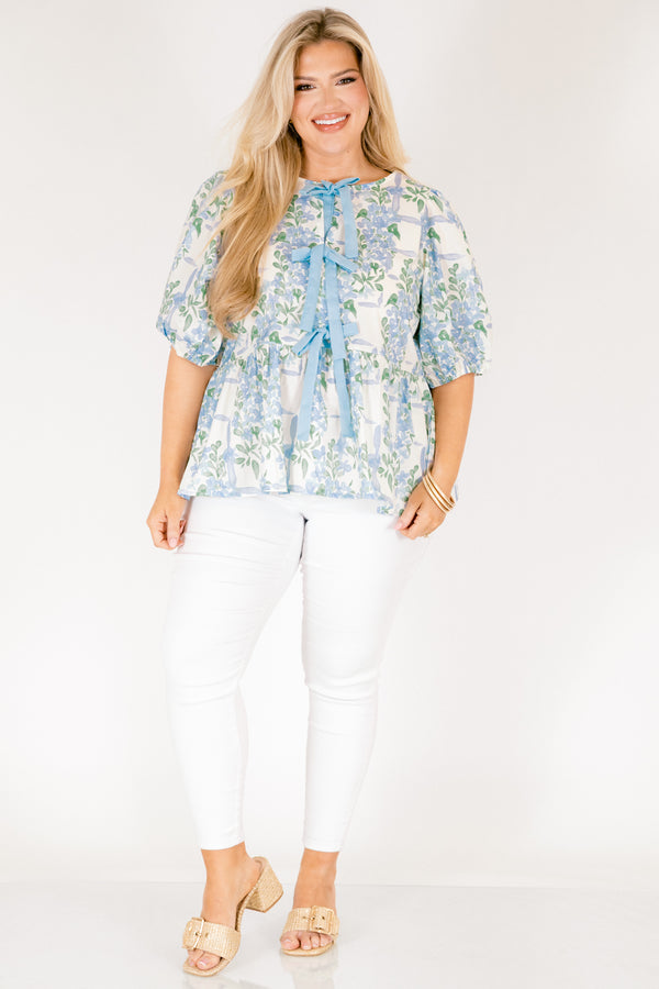 Chic Soul plus size clothing, white puff short sleeve babydoll top with light blue and green floral pattern and three blue bow ties down the middle of the top and cinching at the end of the sleeves