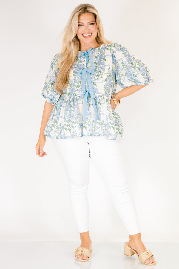 Chic Soul plus size clothing, white puff short sleeve babydoll top with light blue and green floral pattern and three blue bow ties down the middle of the top and cinching at the end of the sleeves