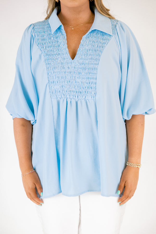 Light blue blouse featuring a split neckline, smocked front detail, and long sleeves with soft gathered cuffs in a lightweight, flowy fabric.