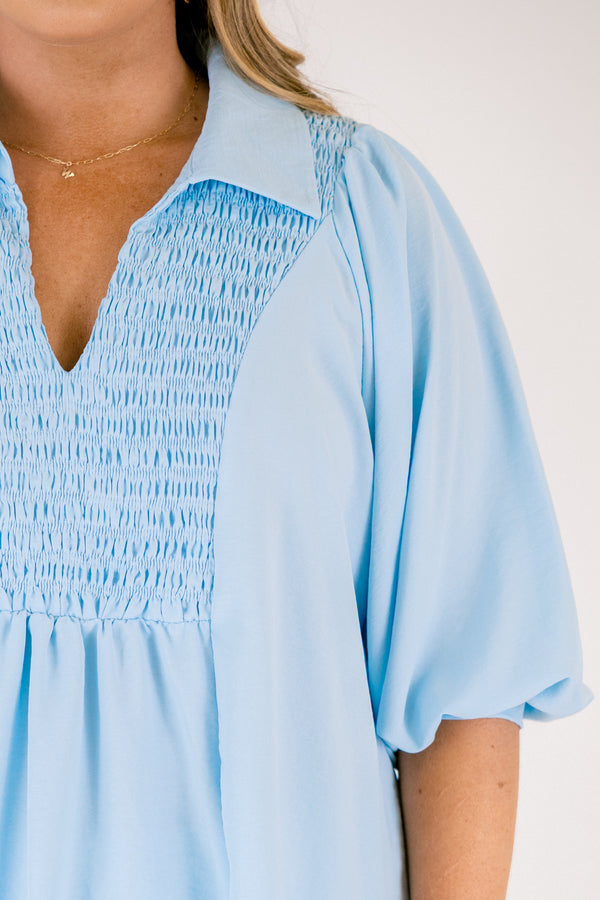 Light blue blouse featuring a split neckline, smocked front detail, and long sleeves with soft gathered cuffs in a lightweight, flowy fabric.