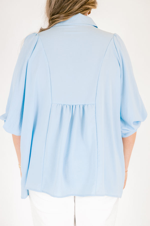 Light blue blouse featuring a split neckline, smocked front detail, and long sleeves with soft gathered cuffs in a lightweight, flowy fabric.