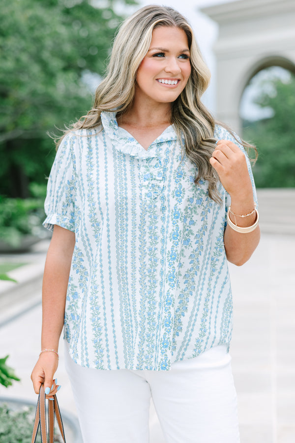 Short-sleeve blue and white floral stripe top with a ruffled button neckline and white pants.
